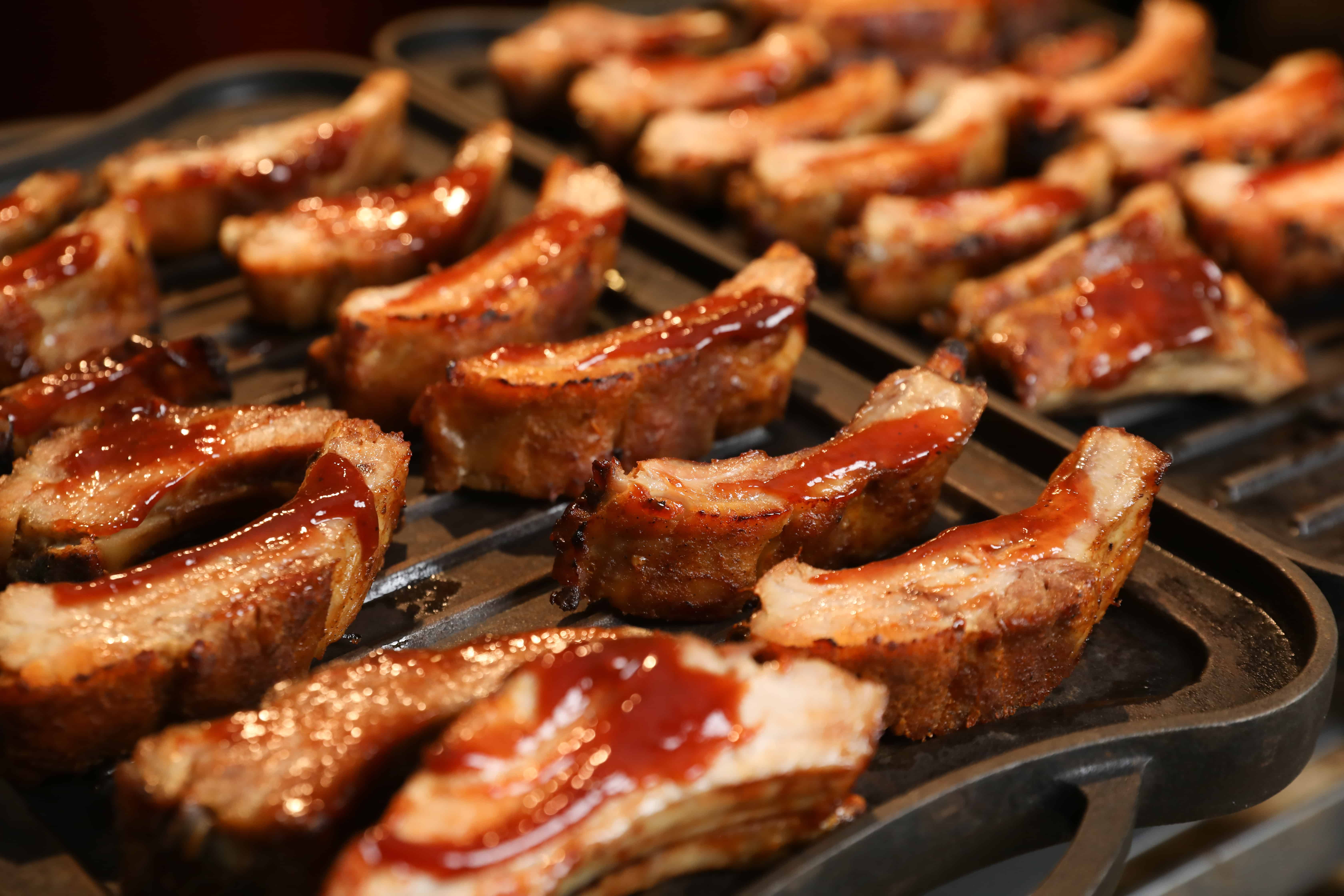 Close-up of a tray of barbecued pork ribs, perfect for catering at wedding venues on Long Island, NY. The ribs are glazed with a glossy, reddish-brown sauce that highlights their juicy and tender texture as they sit evenly spaced on the grill pan, ready to be served.